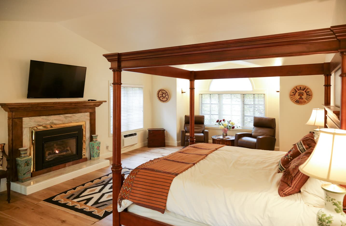 4 poster king size bed in a spacious room with hardwood floors, flat screen tv, and fireplace