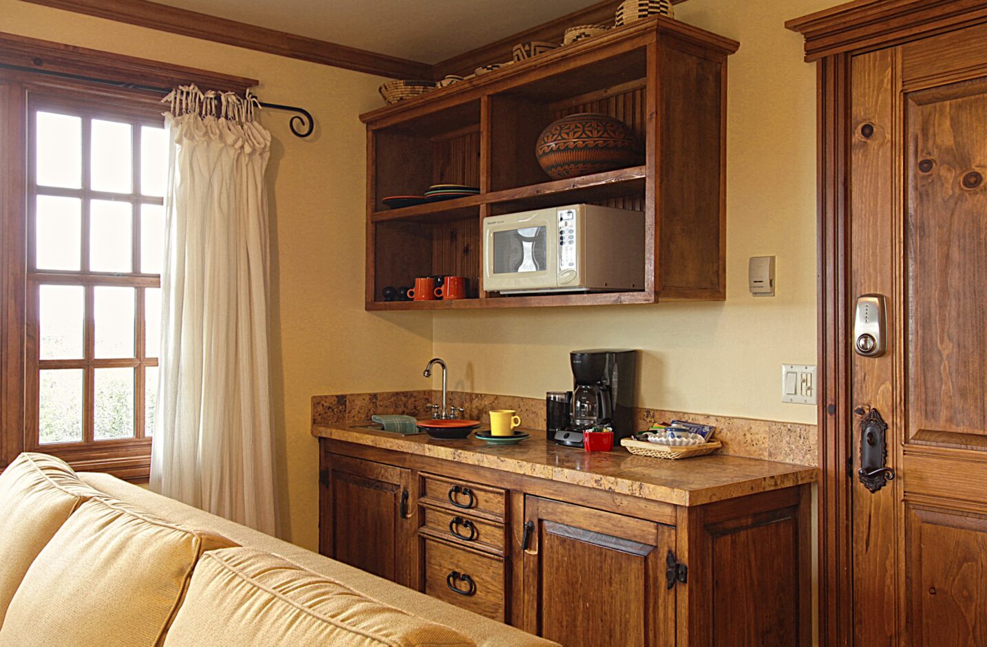 A kitchenette with microwave, coffee pot, and sink. 