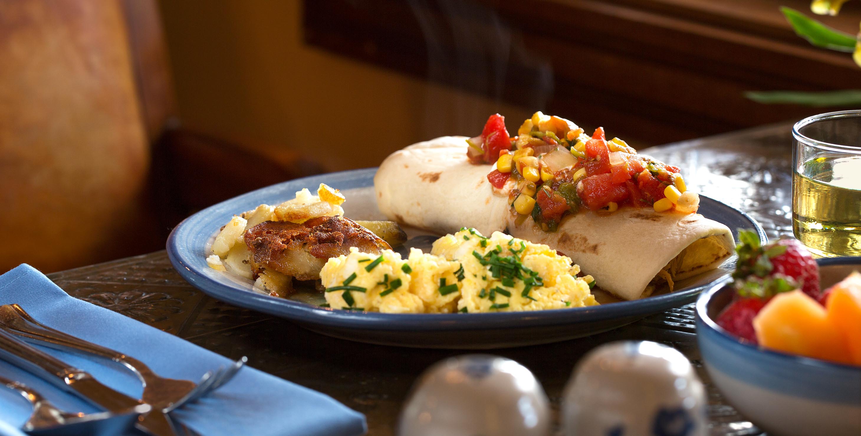 Breakfast burrito topped with corn salsa served with a side of breakfast potatoes and eggs