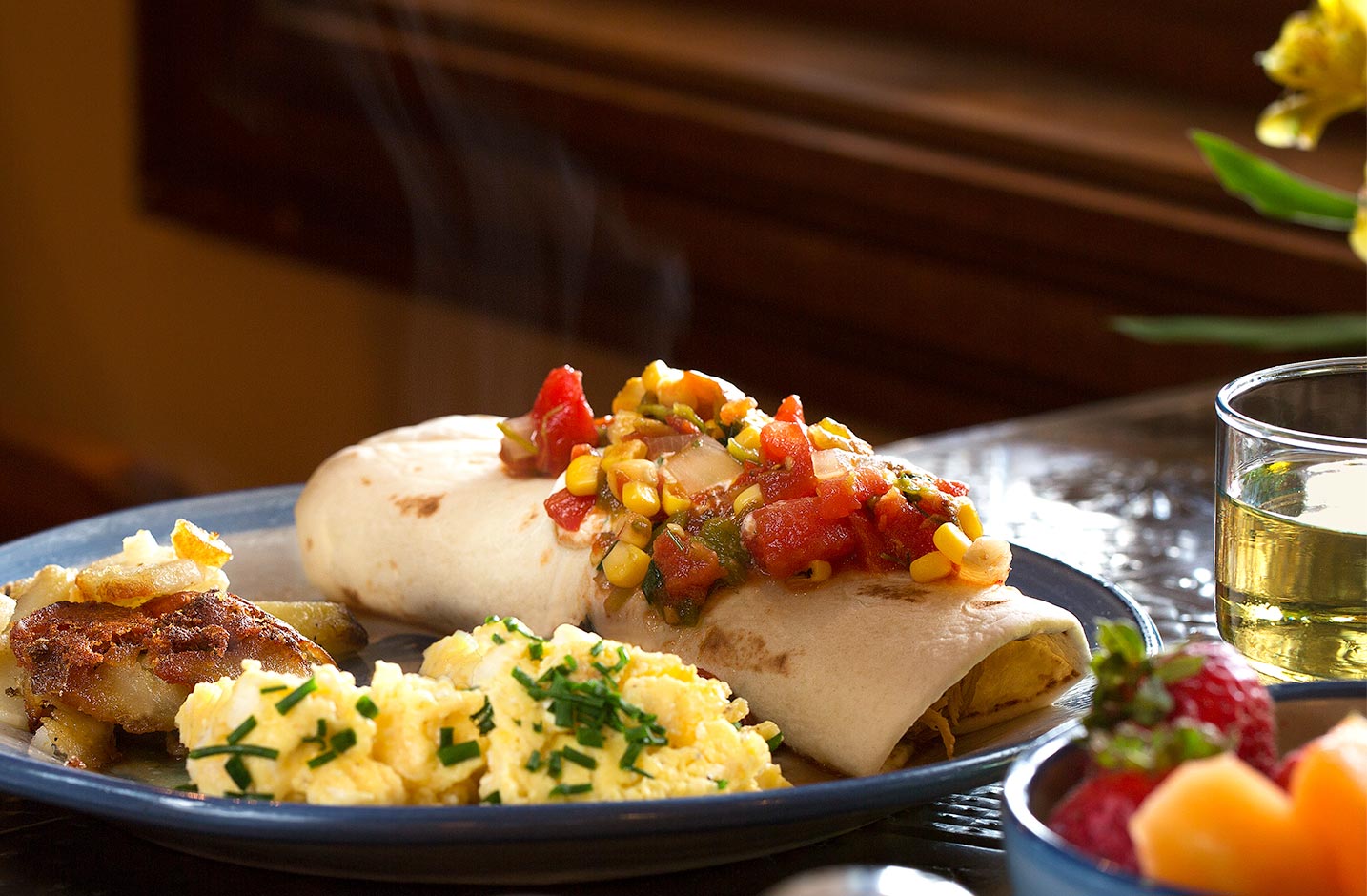 Breakfast burrito topped with corn salsa served with a side of breakfast potatoes and eggs