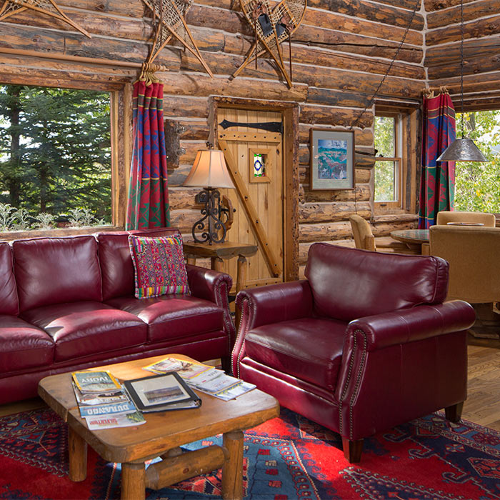 Living room in a log cabin with red leather couches and large windows