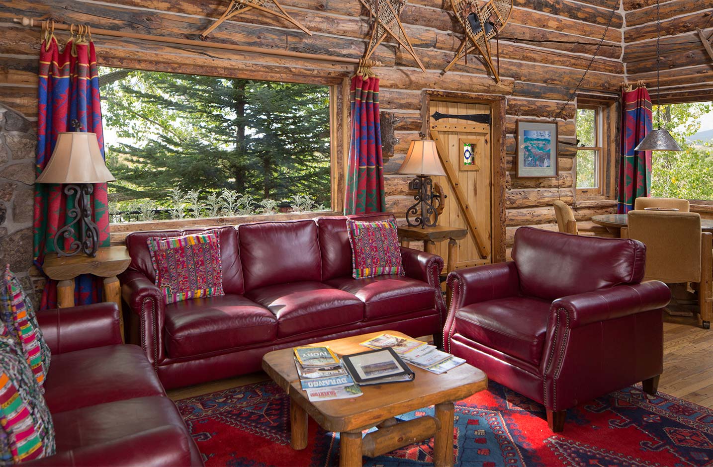 Living room in a log cabin with red leather couches and large windows