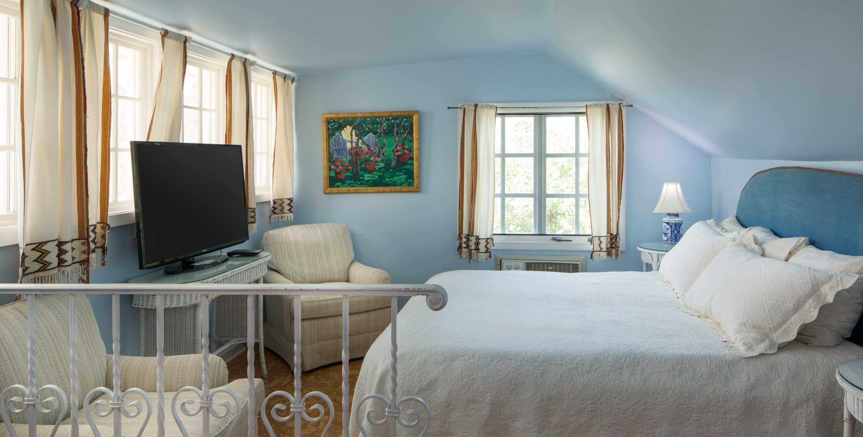 A queen bed and a TV in a room with blue walls and two windows