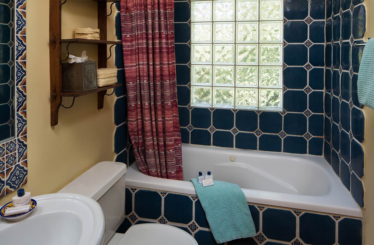 A blue tiled bathroom with large tub and window