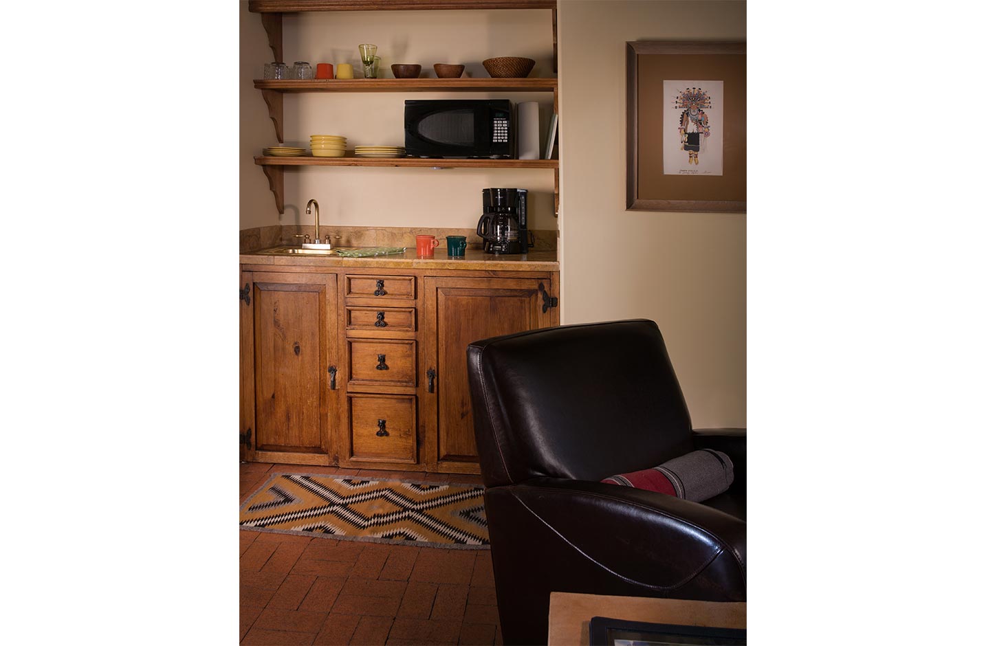 A chair at a writing desk and a wetbar with microwave and coffee maker