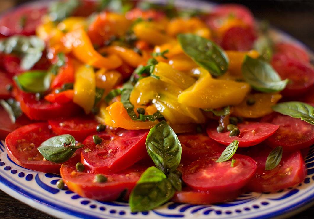 Sliced tomatoes, orange and yellow bell peppers and basil on a plate