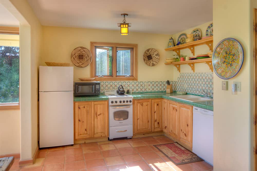 A kitchen with a stove, microwave, fridge, tile floors and counters