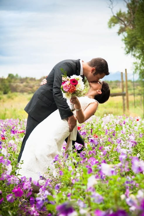 bride and groom kiss while standing in a bed of flowers