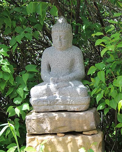 A stone buddha set in front of a green bush